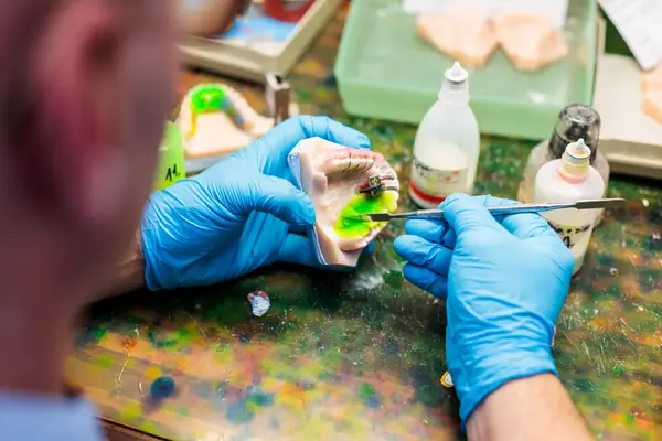 Zahntechniker fertigt Zahnersatz mit Modell und Werkzeugen im Dentallabor an.