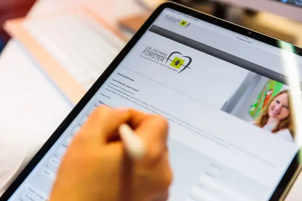 Person füllt digitalen Anamnesebogen für Kieferorthopädie am Tablet in Arztpraxis aus.