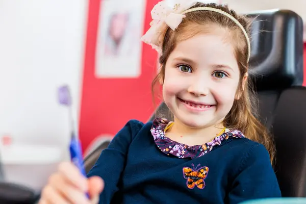 Lächelndes Mädchen beim Zahnarzt hält Zahnbürste, Zahngesundheit für Kinder.